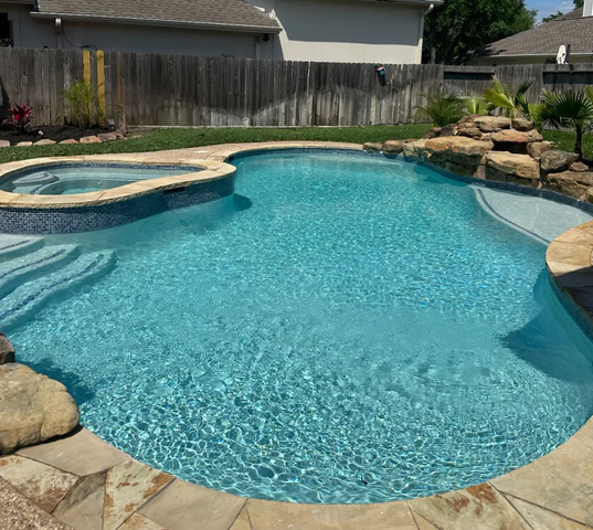 Pool with attached spa, rock waterfall, and travertine deck